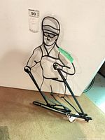 Full view of steel skier silhouette leaning against wall, tag visible