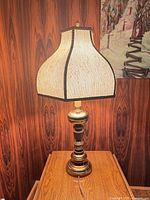 Full view of illuminated brass and wood table lamp with shade on table