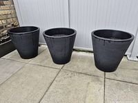 Three black plastic planters lined up on patio