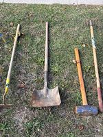 All four long-handled garden tools laid on grass