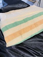 Folded wool blanket showing cream, peach and green stripes on seafoam background