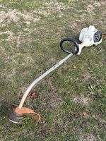 Full view of gas string trimmer lying on grass