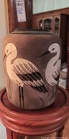 Front view of raku vase showing two cream crackle cranes on matte brown surface