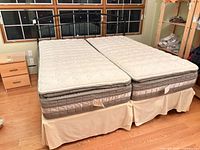 Full view of black metal frame with two Twin XL mattresses and bed skirts