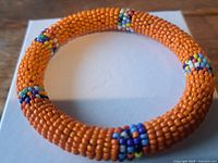 Full view of orange seed bead bangle showing texture and accent bands