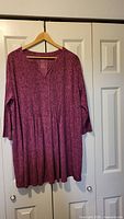 Front view of plum floral tunic on hanger showing V-neck pleats and 3/4 sleeves
