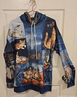 Front view of cat print hoodie on hanger showing graphics, drawstring and pocket