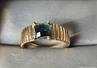 Front view of gold-tone ring showing green rectangular stone and ribbed band