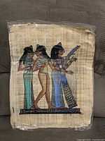 Front view of hand-painted papyrus in protective sleeve, showing three Egyptian women musicians