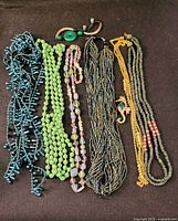 All items laid out showing six necklaces, bracelet at top, seahorse pin on seed bead strands