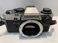 Front view of Olympus OM-10 body showing mount, controls, branding, and strap