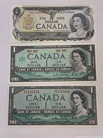 Front views of three Canadian $1 banknotes stacked showing serial numbers, series features and portrait details