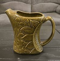 Full side view of olive green floral relief ceramic pitcher