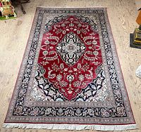 Full view of red Persian Kashan silk rug on wooden floor