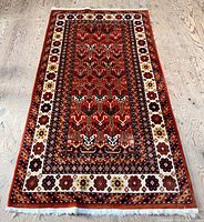 Full view of the rectangular red Turkmen rug laid flat on wood floor
