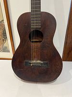 Front view of antique parlor guitar showing body, fingerboard, bridge and soundhole
