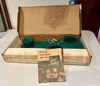 Box opened showing green plastic drink holder, metal clamp parts, and brochure