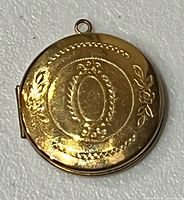 Front view of gold-filled locket showing engraved floral and oval design with bail ring