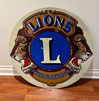 Front view of round metal Lions International sign leaning on wall