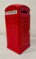 Front view of red ceramic British phone booth piggy bank showing TELEPHONE label and slot