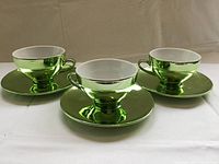 Three green mirrored teacups with saucers displayed