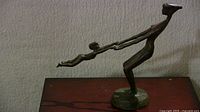 Full side view of bronze sculpture showing female figure leaning back while swinging child