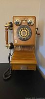 Full view of wooden wall telephone showing handset, crank, bells, dial, and lower storage cabinet