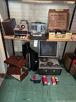 Overall lot showing projectors, reel-to-reel, tripod, bulbs and stand on shelving