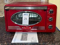 Front view of red Nostalgia Retro Series convection toaster oven with oval glass door and instruction manual