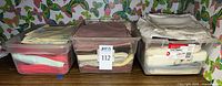 Three storage bins filled with folded linen napkins of assorted colours and styles