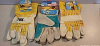Three pairs of gloves laid out: two yellow cowhide, one teal split leather