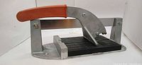 Left side view of tile cutter showing orange grip, aluminum frame, black bed