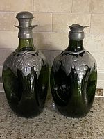 Front view showing both green glass decanters with pewter overlay, one with stopper, one without