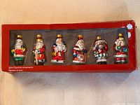 Front view of six glass Santa ornaments in box