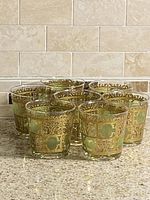 Front view of seven Culver Prado lowball glasses showing green panels and gold filigree