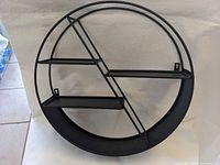 Front view of round black metal wall shelf showing shelves and mounting tabs