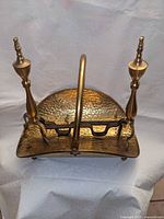 Top view of hammered brass log cradle with arched handle and attached andirons