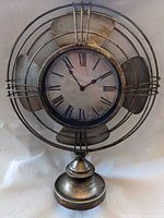 Front view of fan-style metal clock showing antiqued finish and overall form