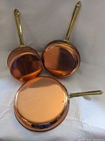 Three copper pans showing exteriors and brass handles