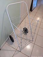 Front angled view of white metal folding grocery cart showing structure and one wheel
