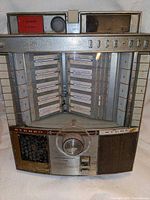 Front view of Rock-Ola song selection wallbox showing full cabinet, selector knob, title strip display