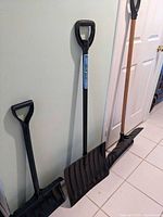 Three snow shovels leaning against wall showing overall condition and size differences.