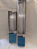 Front view of two boxed chrome towel bars 18 in & 24 in
