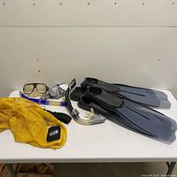Lot overview with fins, snorkels, masks, yellow mesh bag on table