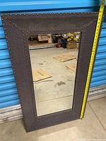 Full view of mirror showing fabric frame, nailhead trim, and tape measure indicating height
