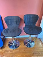Front view of both black upholstered bar stools with chrome bases