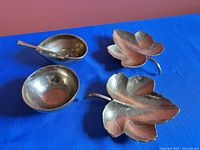 Four brass pieces on blue background: two leaf dishes and two oval bowls with spoon