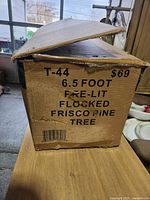 Closed cardboard box showing product label T-44 6.5 foot pre-lit flocked Frisco pine tree