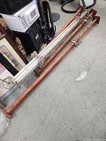 Four telescopic shoring posts laid on floor, two orange steel, one aluminum visible in two sections