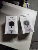 Two Blue by ADT Outdoor Camera boxes front view, one with box damage